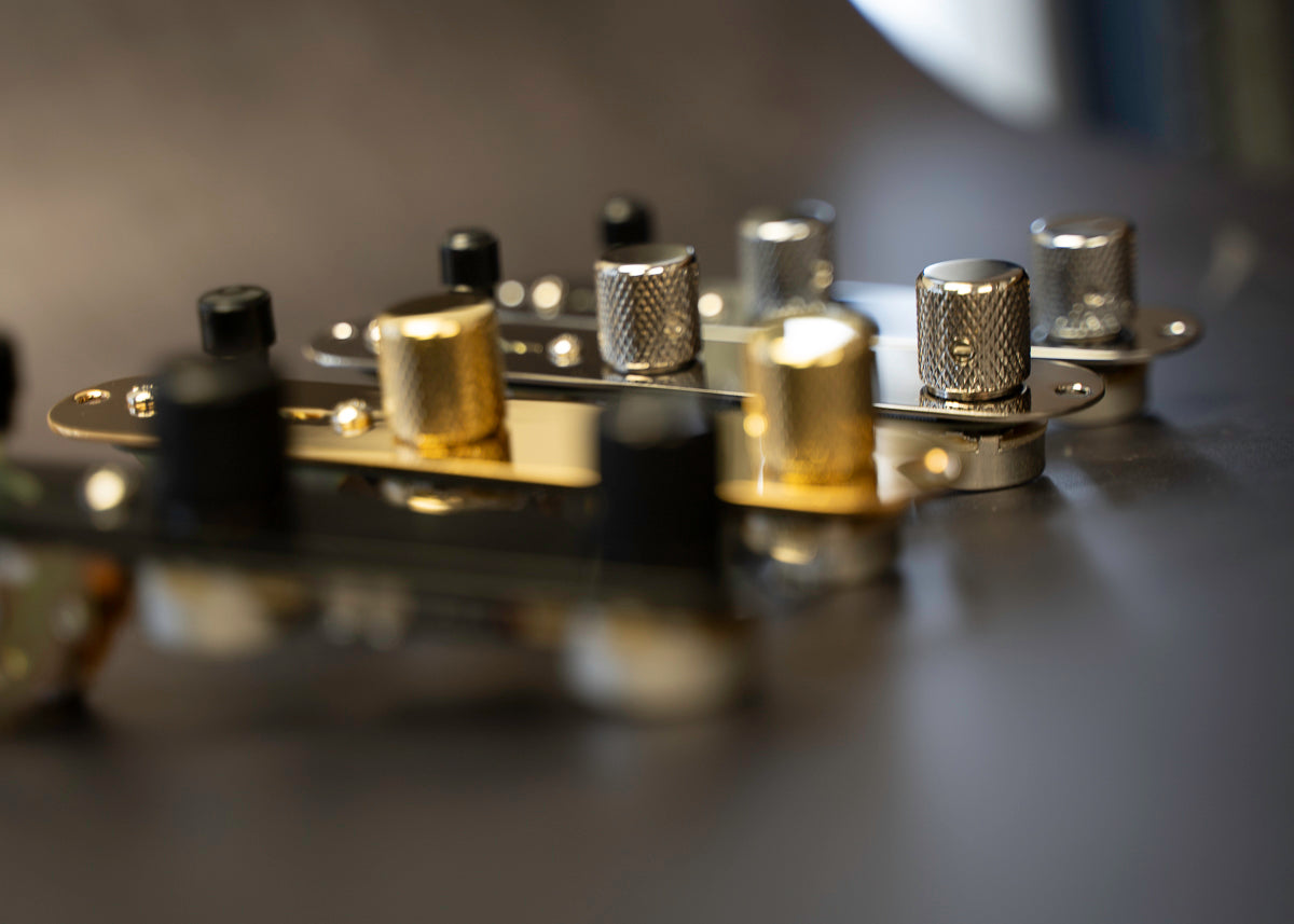 The image shows four loaded control plates for telecaster lined up. Each loaded control plate id finished in a different color with, black, gold, chrome and nickel.