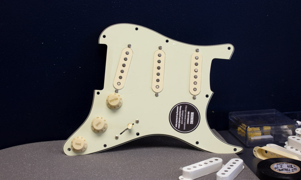 Obsidianwire custom SSS loaded pickguard for Stratocaster. The pickguard is mint green and the knobs and pickup covers are aged white. In the foreground is a stack of spare pickup covers.