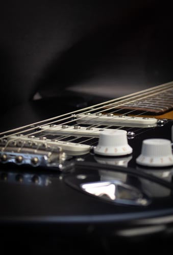 The image shows parchment white knobs and pickup covers on a one ply black pickguard. These are set on a black Fender stratocaster.